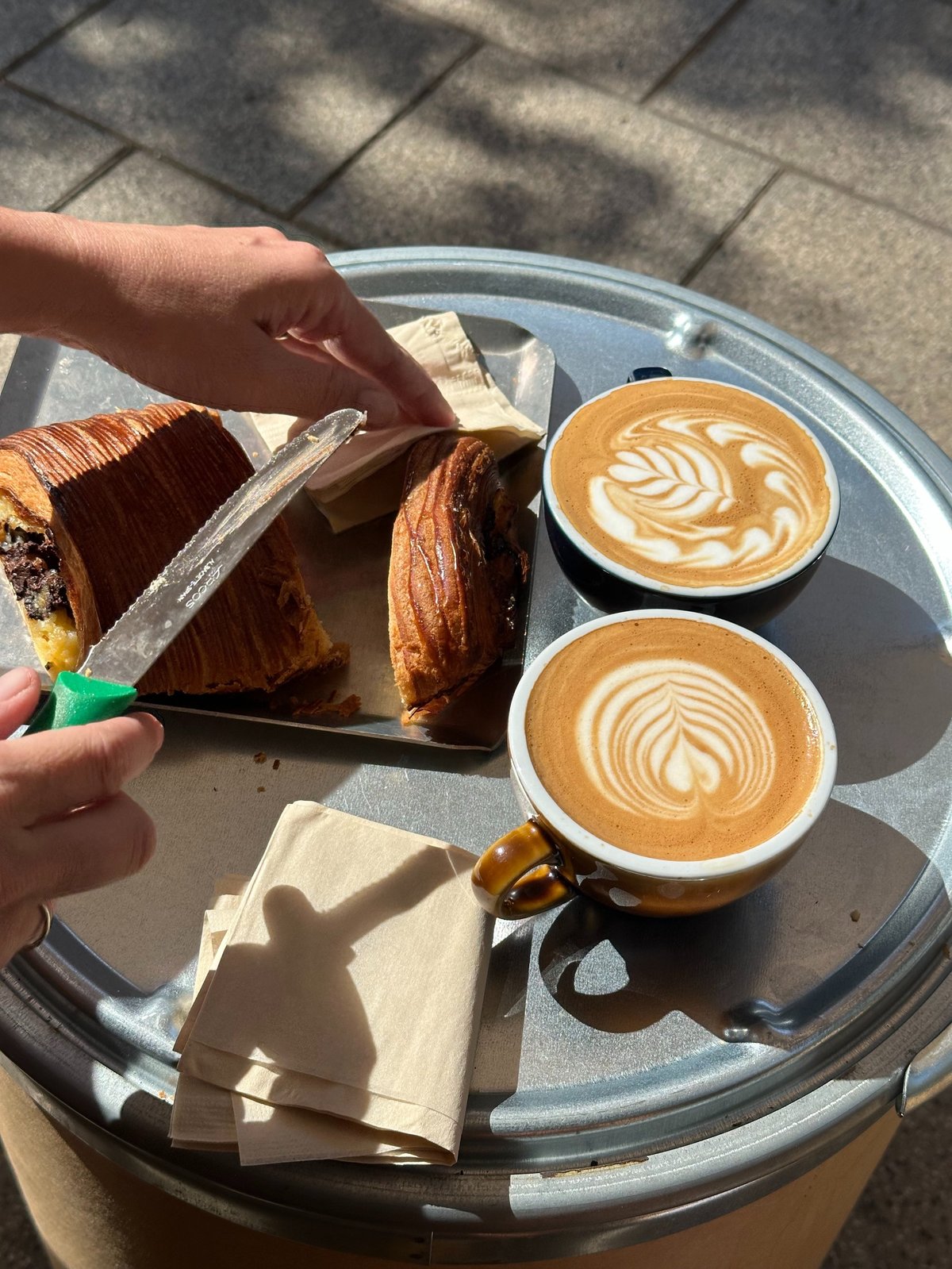 Zwei Tassen Kaffee mit Latte Art und ein frisch gebackenes Gebäck auf einem Tischchen im warmen Morgenlicht